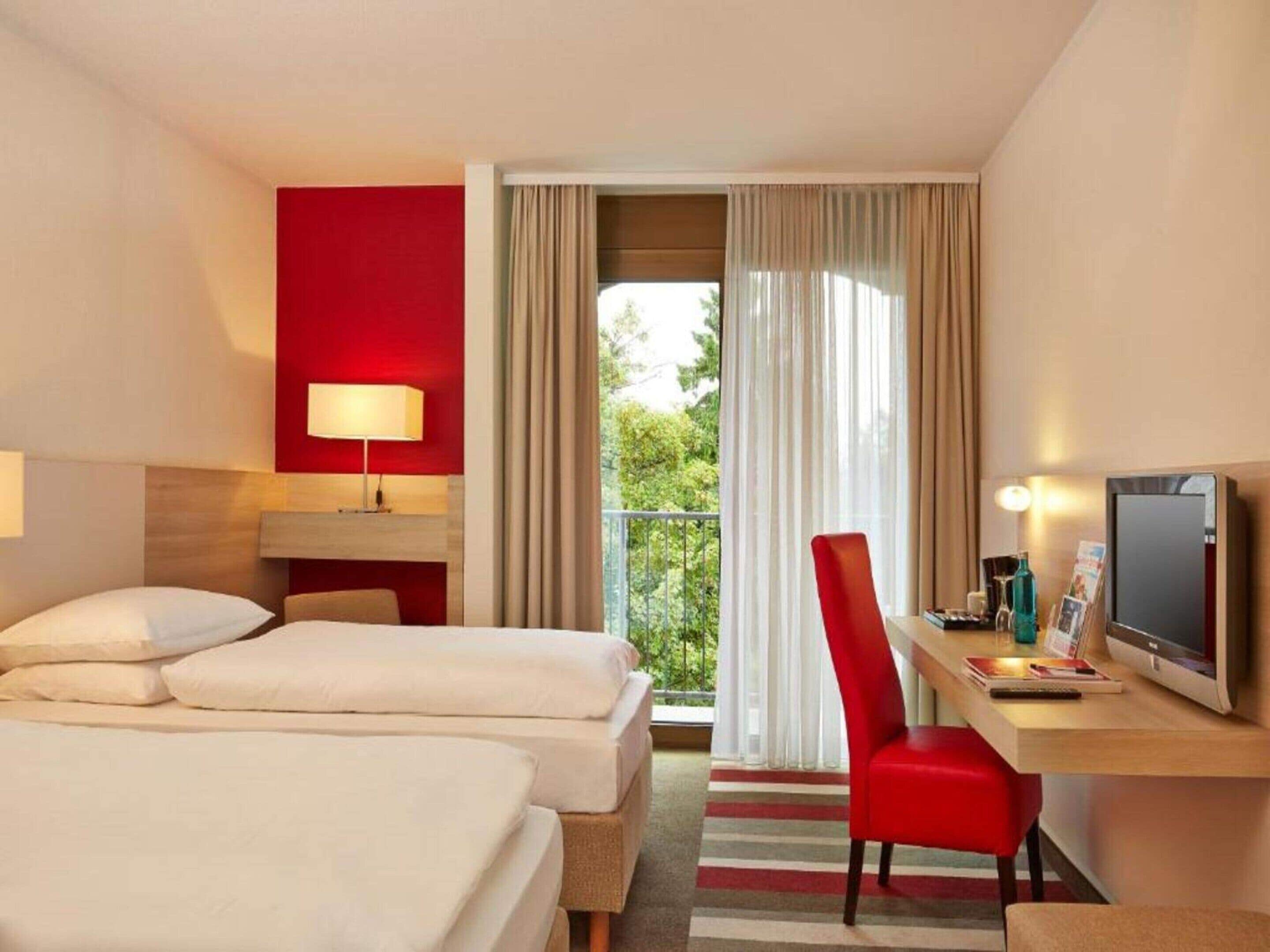 Een hotelkamer met twee bedden, een bureau met stoel, een televisie en een raam met gordijnen.