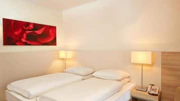 A hotel room with a double bed, two bedside lamps, a wooden nightstand with a phone, and a red flower painting on the wall.