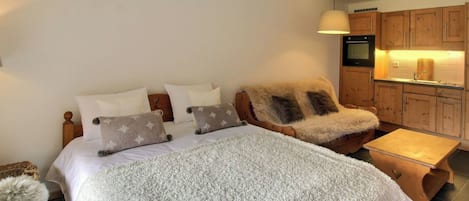 Ein Schlafzimmer mit einem großen Bett, einem Sessel, einem kleinen Tisch und einer Küchenzeile.