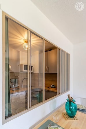 A modern kitchen with a glass partition, a teal vase, and a dining table with a glass. - Ô Lago - AIX-LES-BAINS (AIX LES BAINS)
