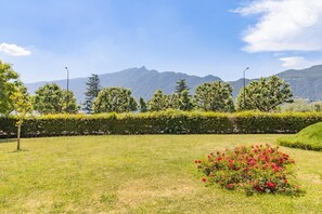 A landscaped garden with a hedge, a flower bed, and a view of mountains. - Ô Lago - AIX-LES-BAINS (AIX LES BAINS)