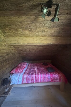 Ein kleines Zimmer mit einem Einzelbett, geneigter Decke und Holzwänden.