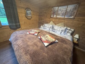 A cozy wooden room with a large bed, two pillows, a framed picture, and a window with a view. - La Chotte du Musher, (Champery), by Interhome (Champery)