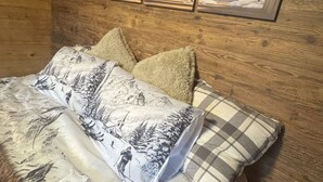 A wooden cabin room with a bed, pillows, a painting of a snowy mountain landscape, and a lamp on a nightstand. - La Chotte du Musher, (Champery), by Interhome (Champery)