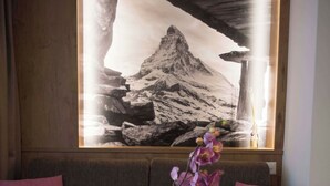 A room with a wooden table, a vase with flowers, and a large framed picture on the wall. - Patricia self-check-in Apartments, (Zermatt), by Interhome (Zermatt)