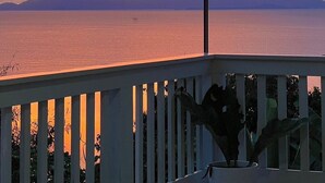 A sunset view from a covered balcony with a railing and a potted plant.