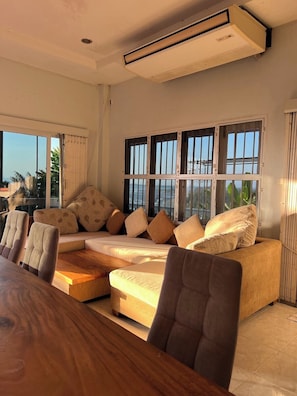 Una sala de estar moderna con un conjunto de sofá, una mesa de comedor y ventanas amplias con barandillas.
