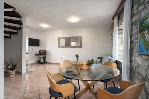 A dining area with a glass table and wooden chairs, a television on the wall, a stone wall, and a staircase. - Holiday apartment near Poreč with a beautiful panoramic view (Poreč)