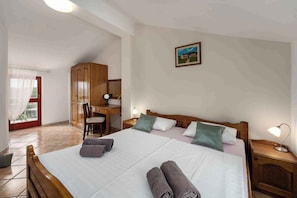 Ein Schlafzimmer mit Bett, Nachttischen, Schreibtisch, Stuhl, Kleiderschrank und einem Fenster mit Vorhängen.