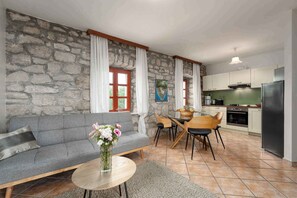 A living room with a grey sofa, a round coffee table with a vase of flowers, and a dining area with wooden chairs and a table. - Holiday apartment near Poreč with a beautiful panoramic view (Poreč)