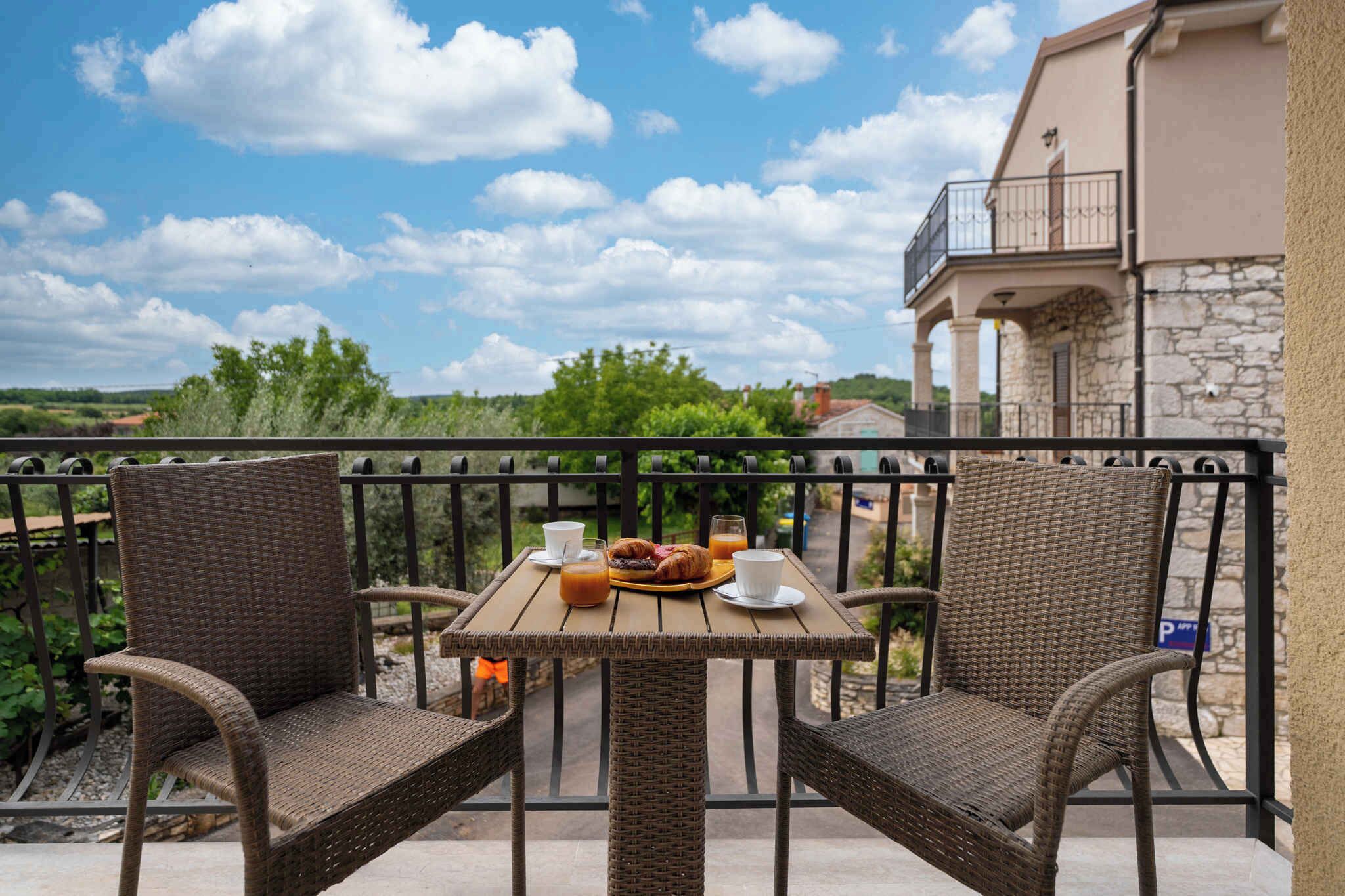 A balcony with wicker chairs, a table with breakfast, and a view of the countryside.