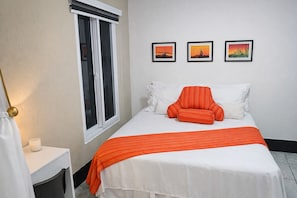 Une chambre à coucher avec un lit, une fenêtre, une table de chevet et trois tableaux encadrés accrochés au mur.