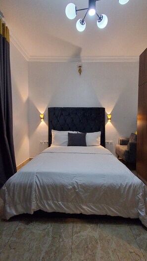 Ein großes Bett mit dunklem Kopfteil, zwei Wandleuchten und einer Deckenlampe.