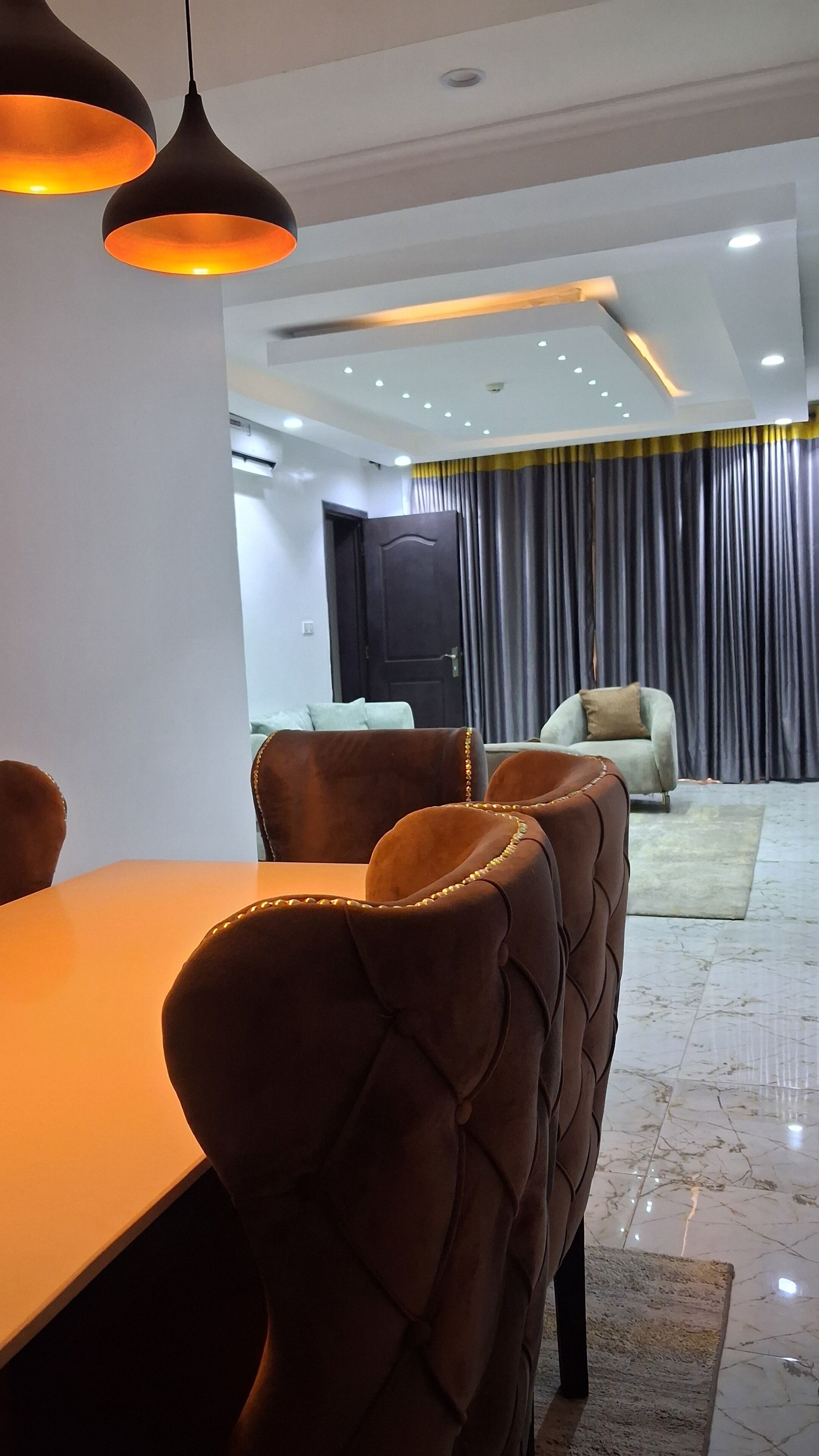 A dining area with a table and chairs, a sofa, a curtain, and a door in the background.