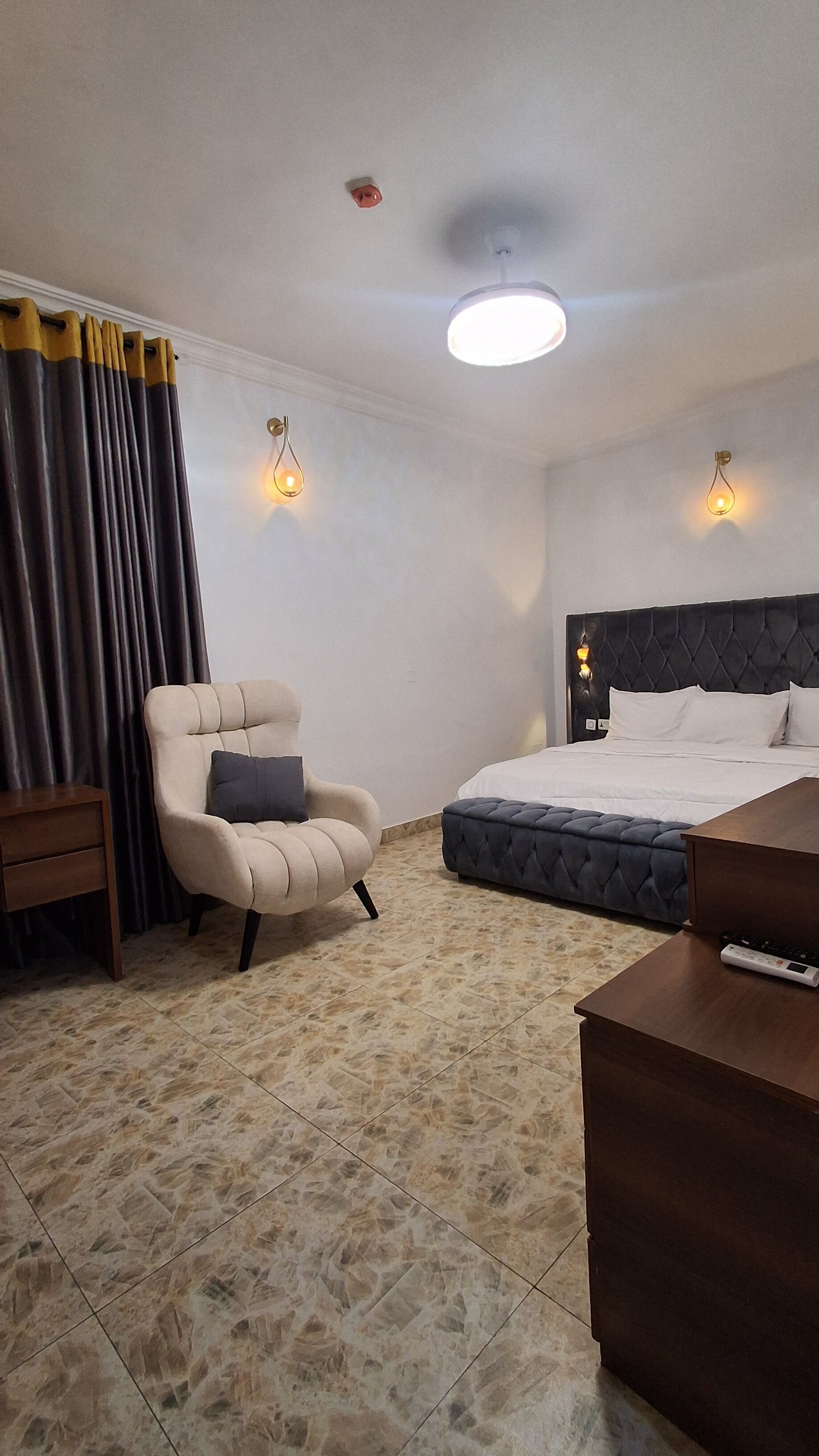 A hotel room with a bed, a chair, a bedside table, a lamp, and a ceiling light.