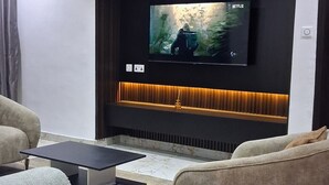 Ett modernt vardagsrum med en platt-TV som är monterad på en mörk vägg, ett svart soffbord, två soffor och en mönstrad matta.