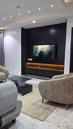 A modern living room with a flat-screen TV mounted on a dark wall, a black coffee table, two sofas, and a patterned rug. - Lovely Spacious 3-bedroom apartment with AC in awesome Lagos, 15min from Airport (Lagos)