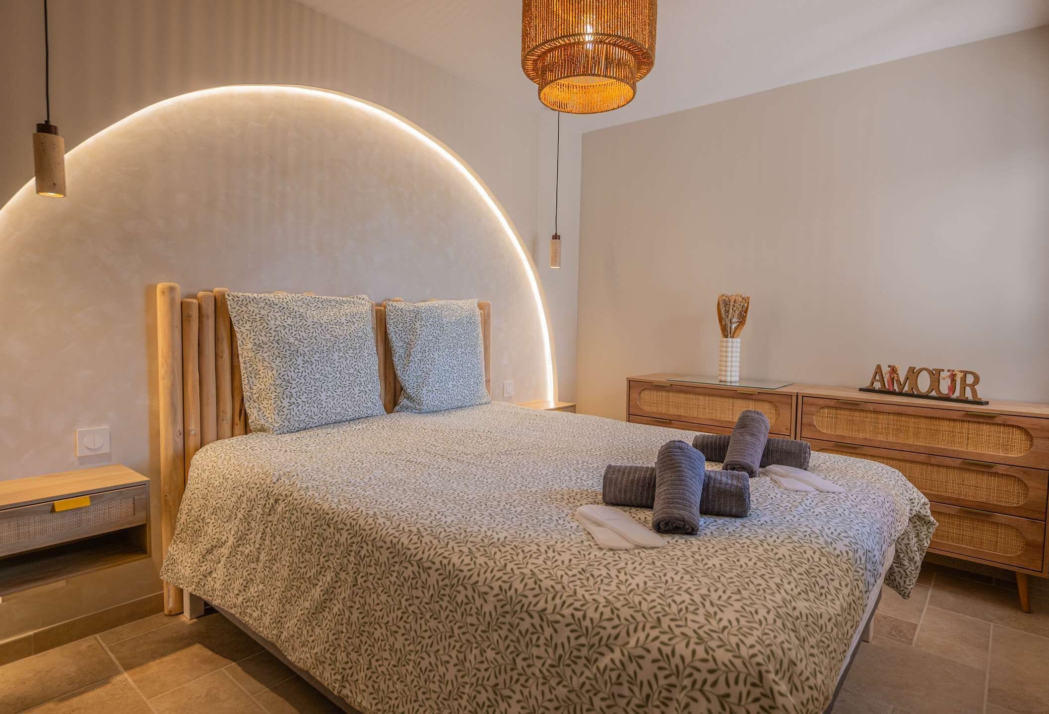 A modern bedroom with a curved headboard, a bedside table, a wooden dresser, and a decorative item on the dresser.