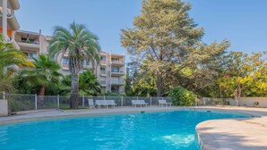 A swimming pool with a curved edge, surrounded by a fence, and adjacent to a multi-story building with balconies. - BRAND-NEW APARTMENT - SWIMMING POOL - PRIVATE PARKING - WALKING DISTANCE TO THE TOWN CENTRE AND... (STE MAXIME)