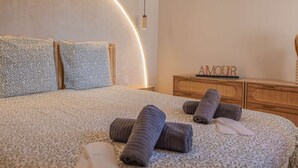 A modern bedroom with a curved headboard, a wooden dresser, and rolled towels on the bed. - BRAND-NEW APARTMENT - SWIMMING POOL - PRIVATE PARKING - WALKING DISTANCE TO THE TOWN CENTRE AND... (STE MAXIME)