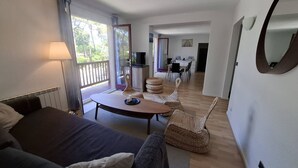 Uma sala moderna com sofá, mesa de centro redonda, cadeiras de vime, televisão e área de jantar com mesa e cadeiras.