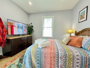 A bedroom with a bed, a TV on a dresser, a window, and a lamp.