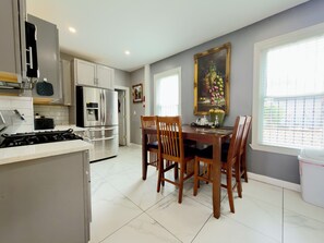 A modern kitchen with white cabinets, a stainless steel refrigerator, and a dining area with wooden chairs and a table.
