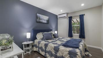 A bedroom with a bed, bedside tables, a nightstand, a window with curtains, and an air conditioning unit.
