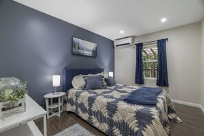 Ein Schlafzimmer mit Bett, Nachttischen, einem Fenster mit Vorhängen und einer Klimaanlage.