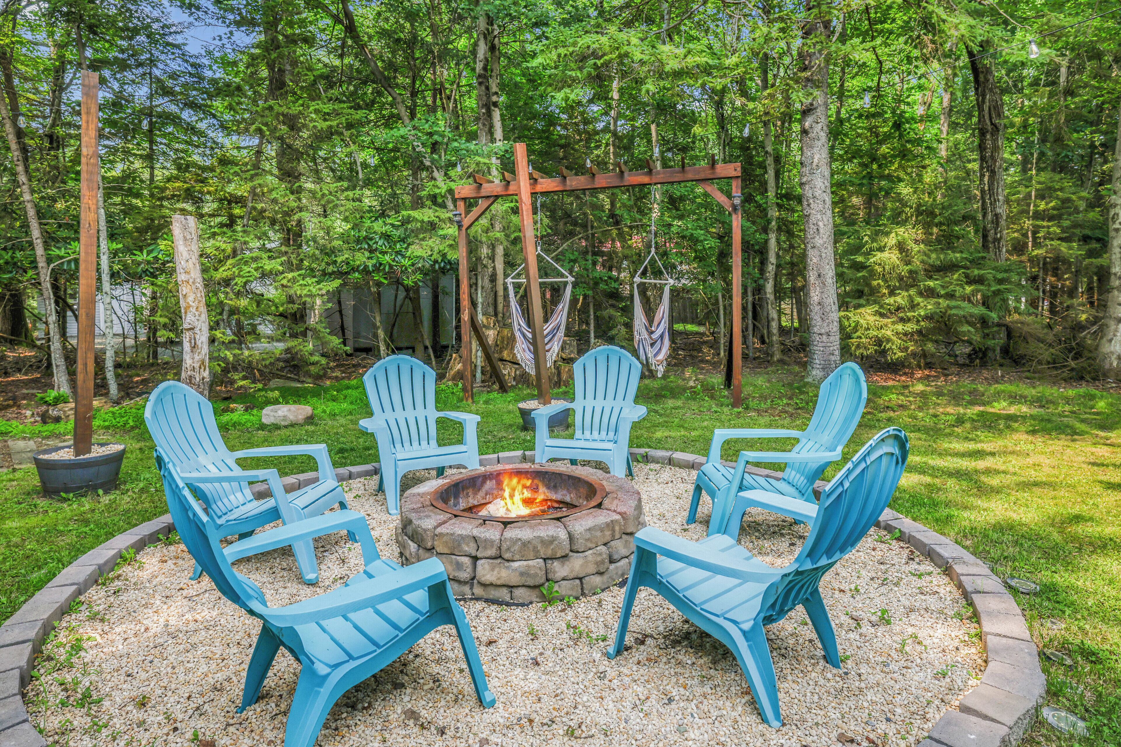 A circular seating arrangement around a fire pit with four chairs, surrounded by a gravel area and a wooden pergola.