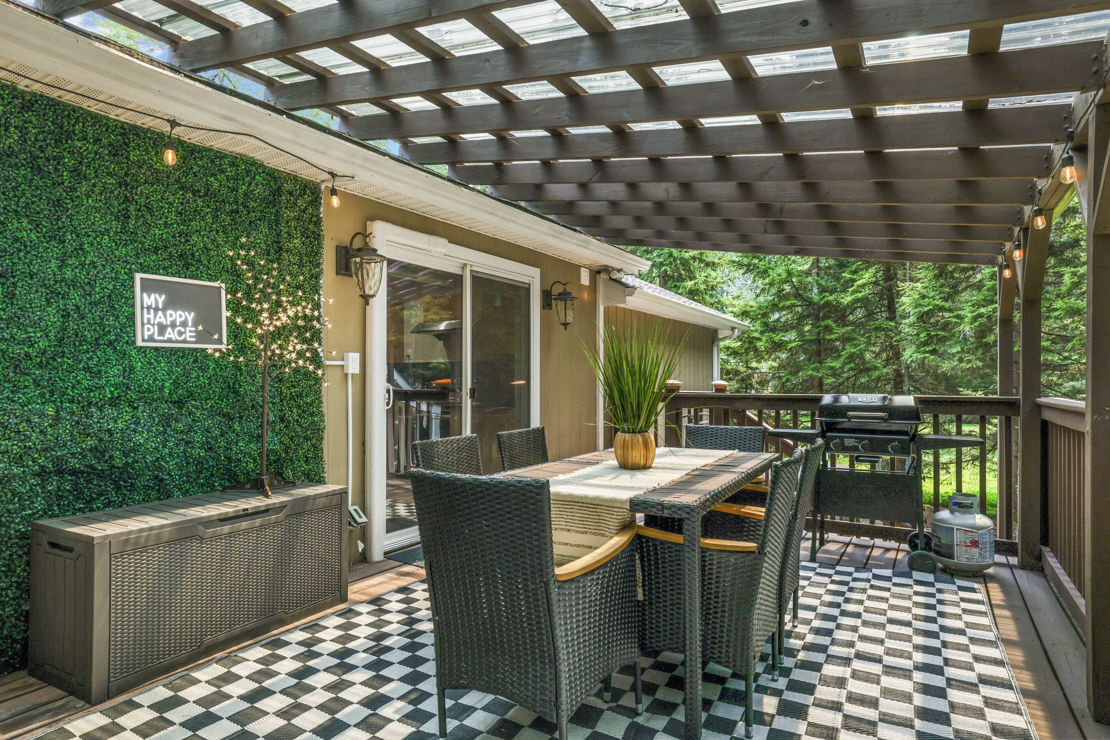 An outdoor patio with a checkered floor, wicker furniture, a grill, and a wall with a 'MY HAPPY PLACE' sign.