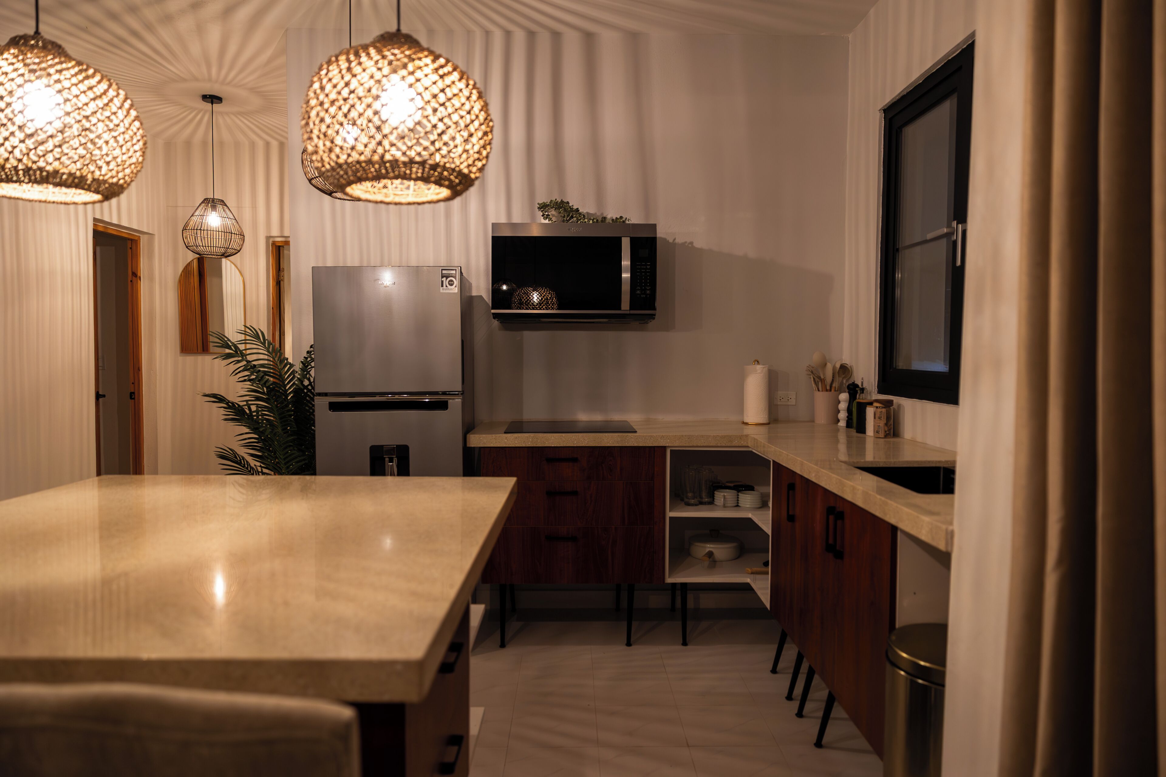 Een moderne keuken met een marmeren aanrechtblad, houten keukenkastjes, een ingebouwde magnetron en hangende lampen.