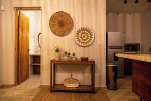 A hallway with a wooden door, a console table with decorative items, and a kitchen area with a refrigerator and microwave.