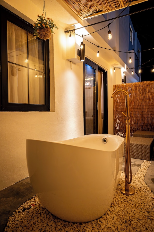 A large bathtub in an outdoor setting with string lights and a hanging flower basket.