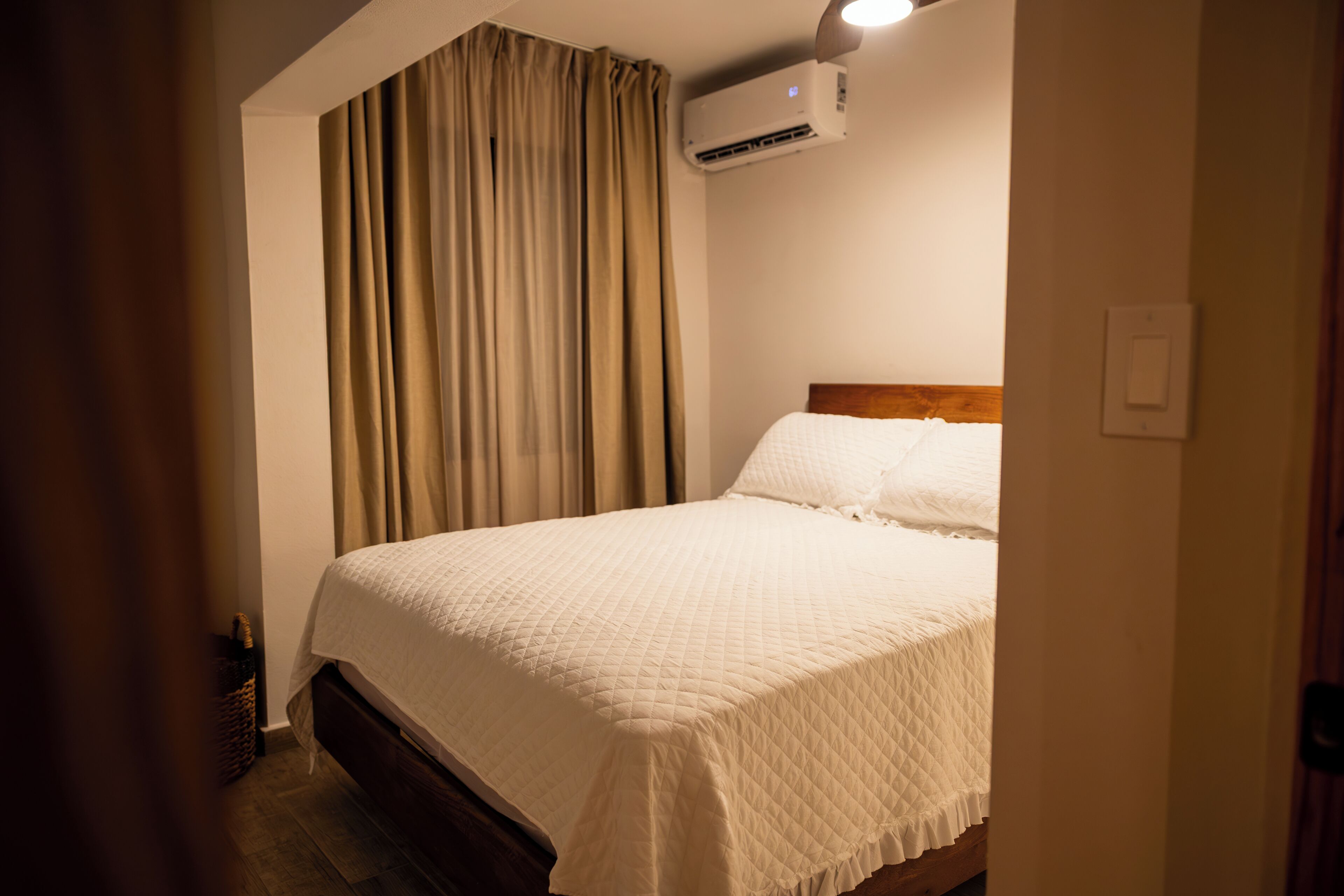 Habitación de hotel con cama, cortinas, aire acondicionado y cabecera de madera.