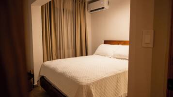Habitación de hotel con cama, cortinas, aire acondicionado y cabecera de madera.
