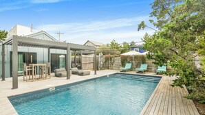 Une piscine avec une terrasse en bois, un espace salon couvert et une cour arrière clôturée.