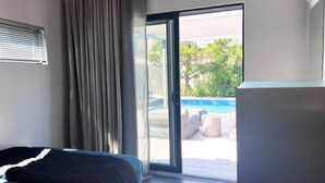 Une chambre avec un lit et une porte-fenêtre coulissante donnant sur un espace extérieur comprenant une piscine et du mobilier.