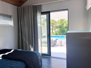 Ein Schlafzimmer mit einem Bett, einer Schiebetür zu einem Außenbereich mit Pool und Möbeln.