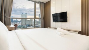 Habitación de hotel con una cama grande, un televisor montado en la pared y vistas a la ciudad por la ventana.