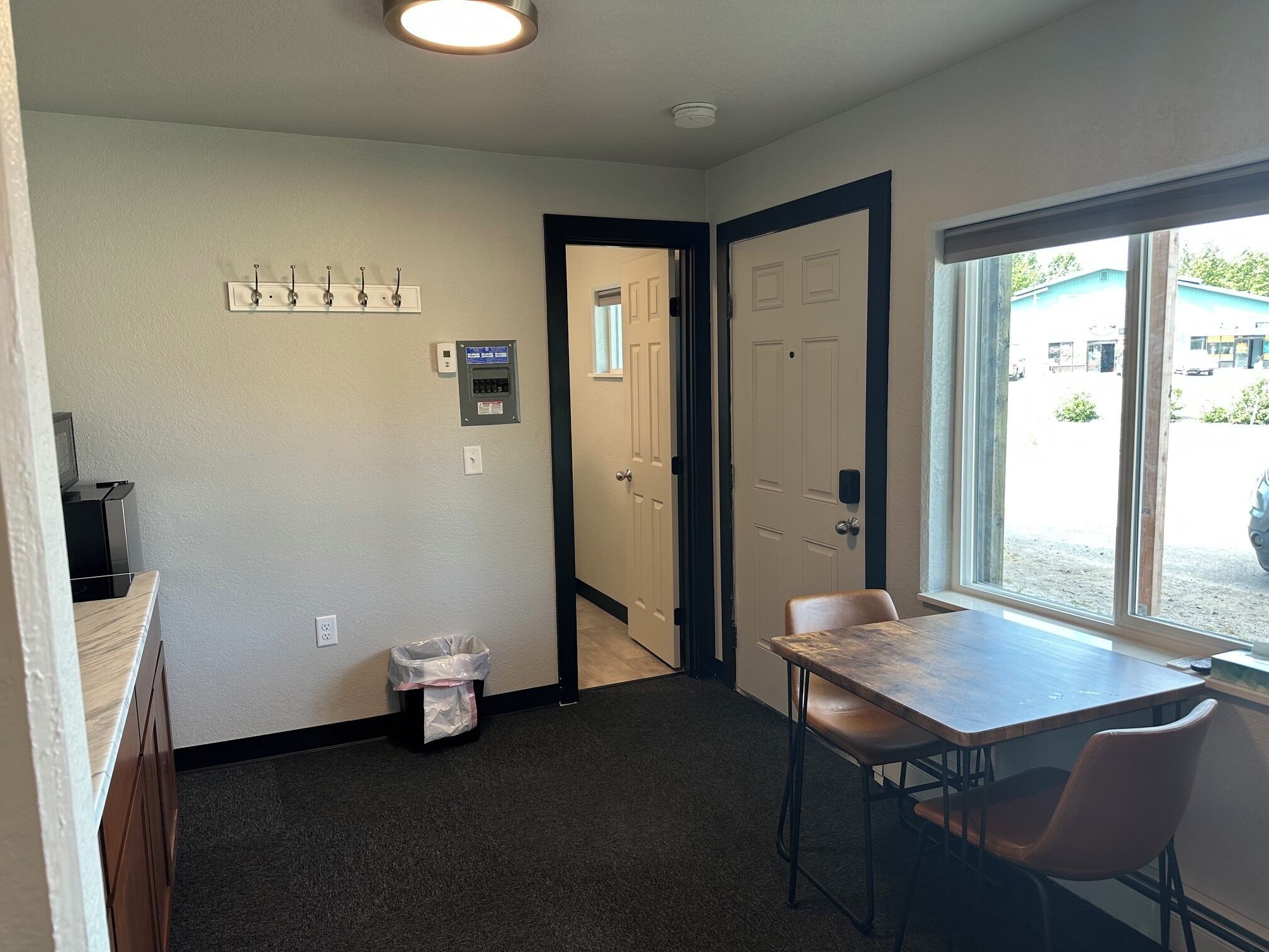 A room with a table and chairs, a window, a door, and a wall-mounted electrical panel.