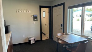 A room with a table and chairs, a window, a door, and a wall-mounted electrical panel. - Room 20. Angry Salmon Inn. (Anchor Point)