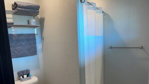 A bathroom with a toilet, a shower with a glass door, a towel rack with folded towels, and a shelf with toiletries. - Room 20. Angry Salmon Inn. (Anchor Point)