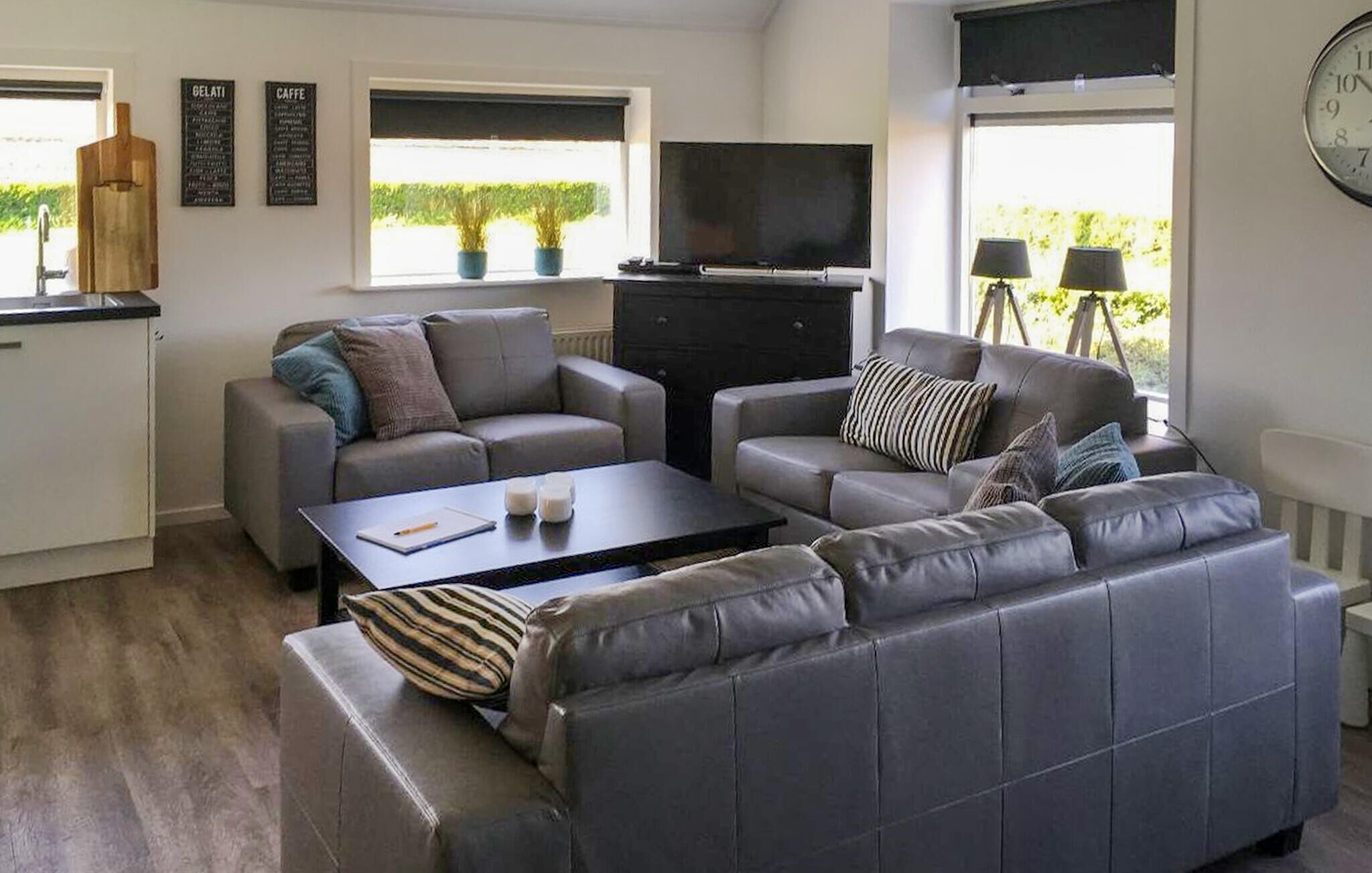 A modern living room with a grey sofa set, a flat-screen TV, and a coffee machine.