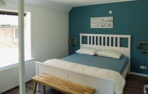 Ein Schlafzimmer mit einem weißen Bett, einer hölzernen Bank, einer blauen Wand und einem Fenster.