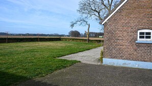 A brick building with a window and a door, a grassy yard, and a hedge. - 5 bedroom nice home in Schalkhaar (Schalkhaar)