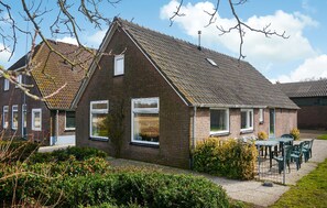 Ein zweistöckiges Backsteinhhaus mit Satteldach, einem sichtbaren Schornstein und einem kleinen Garten mit Tisch und Stühlen.