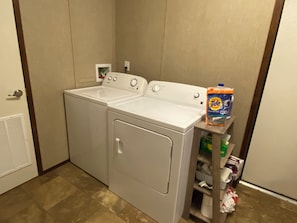 A laundry area with a front-loading washer and dryer, a shelf with Tide detergent, and a vent on the left.