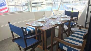 A dining area with a table set for four, chairs with blue cushions, and a view of boats through large windows.