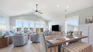 Ein geräumiges Wohnzimmer mit Essbereich, großen Fenstern und einem Deckenventilator.